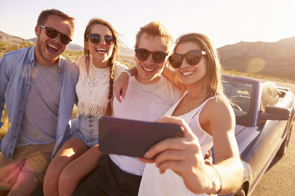 Friends taking a selfie sat on the front of a car